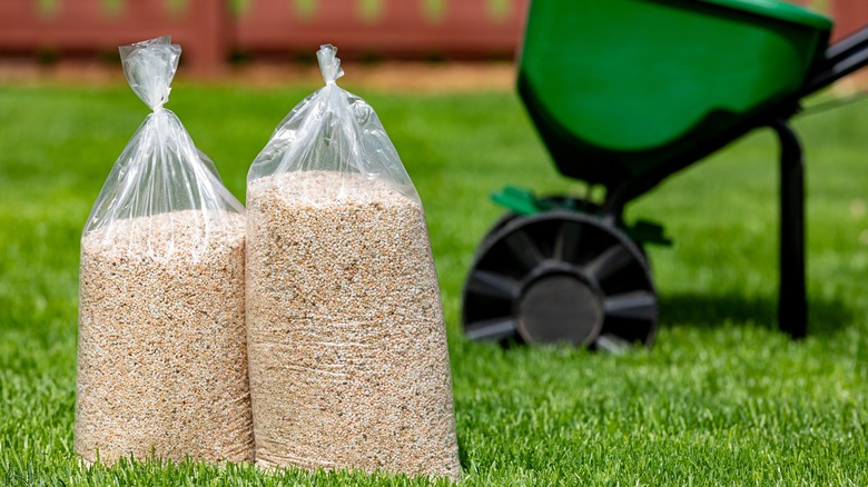 Bags of fertilizer sitting on the lawn next to a broadcast spreader