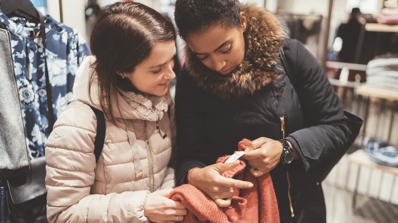 Two people checking the price tag on a sweater