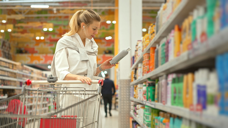 person in the aisle of a large store holding a bottle of shampoo