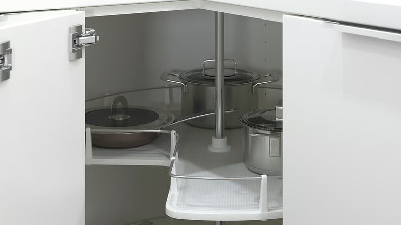 Corner kitchen cabinet carousel with stainless steel cooking pots and lids