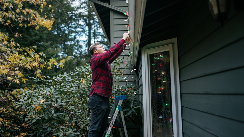 Man on a ladder putting string lights on house
