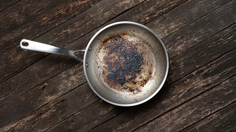 A dirty aluminum frying pan on a wood background.