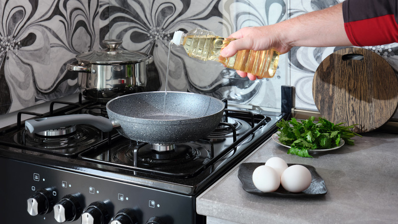 A person pouring oil onto a nonstick frying pan on a gas stove.