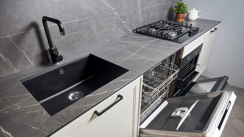 Dark-colored, quartz-patterend poreclain countertop with a black sink and new kitchen appliances.