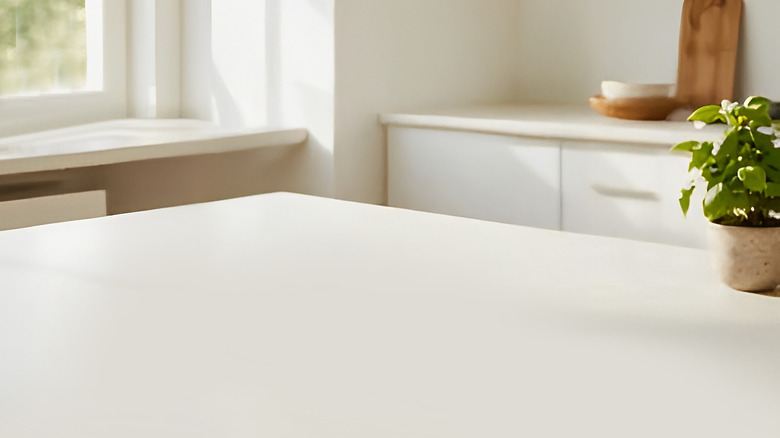 A kitchen with pure white quartz countertops adorned with cooking accessories and a pot plant.