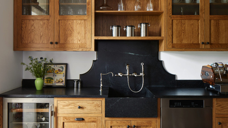 Dark soapstone counter and backsplash with a farmhouse sink wood cabinets, and stainless steel appliances.