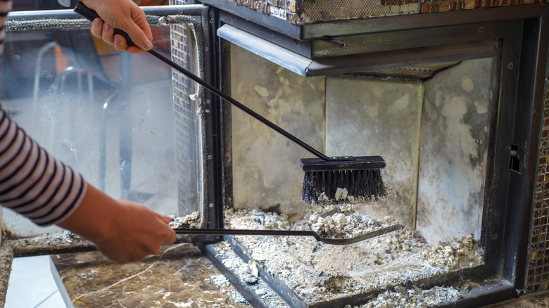 someone scooping out wood ash from fire place with shovel and broom