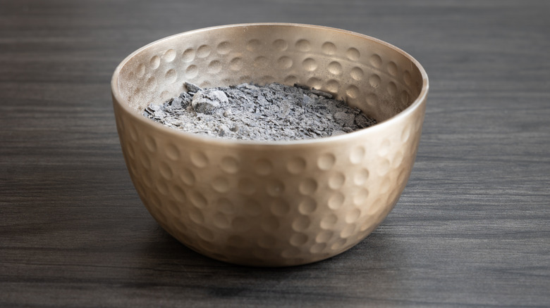 bronze indented bowl with wood ash on brown countertop