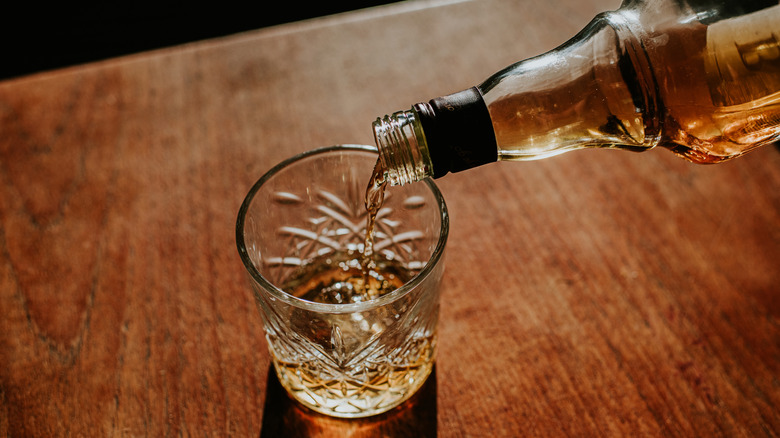 Person pouring whiskey from a bottle into a glass