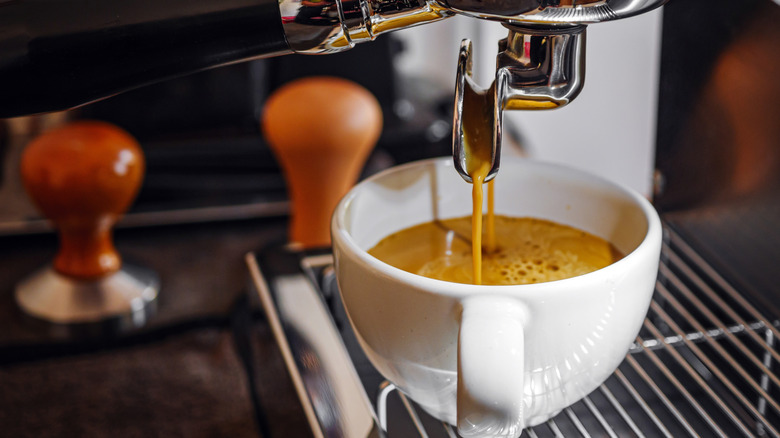 An espresso machine pouring coffee into a white mug