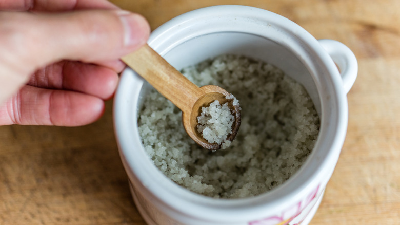 Hand holding spoonful of salt in wooden spoon