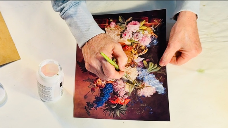 Crafter brushes a coat of decoupage medium over an art print.