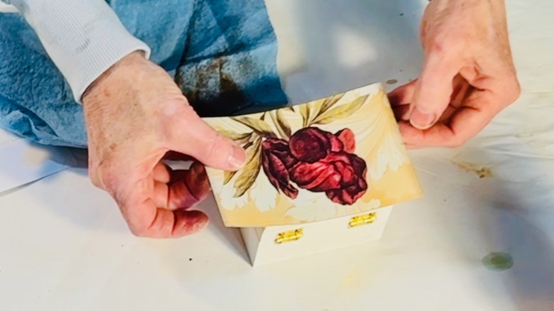 Crafter places a piece she has cropped out of a print and prepares to decoupage it to a box.