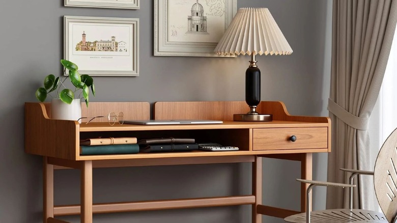 Mid-century style mid-toned wood desk against gray wall with fluted desk lamp