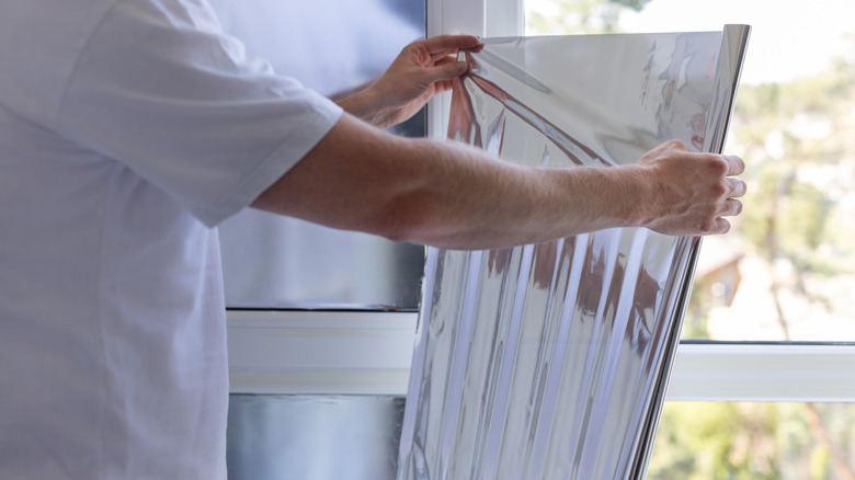 Man unrolling aluminum foil near window
