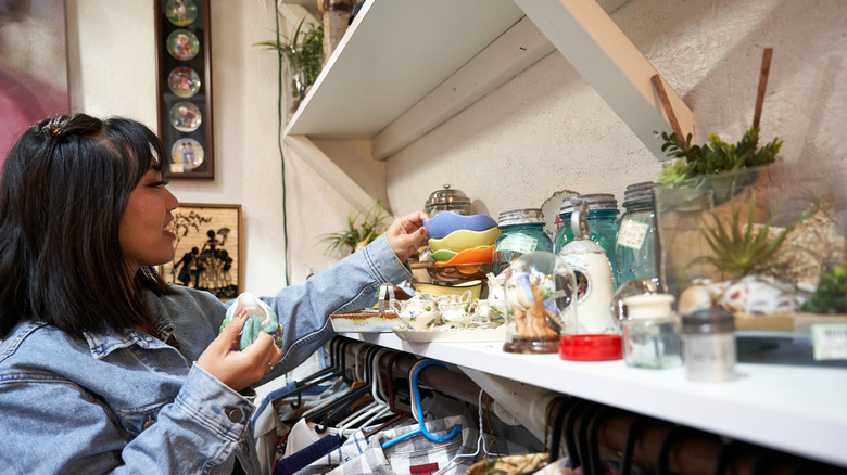 A woman grabs an object off of a thrift store shelf