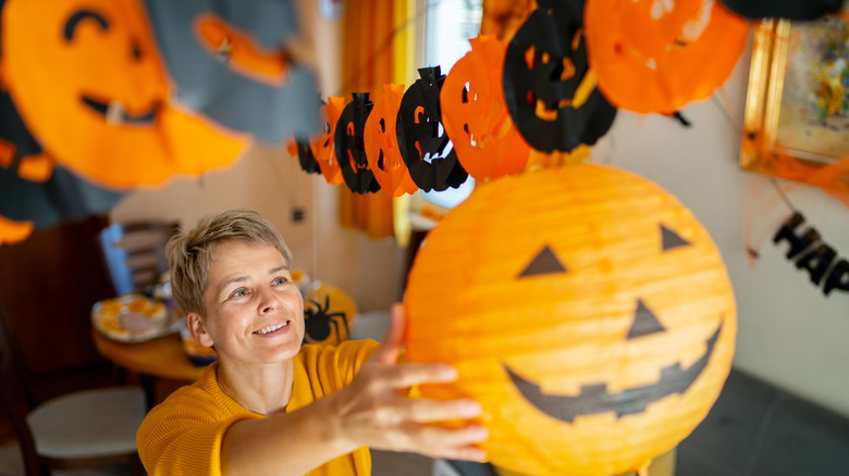 smiling person hangs paper Jacko lantern up for party