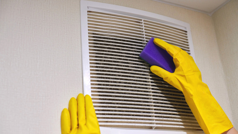 Person cleaning dirty air vent cover