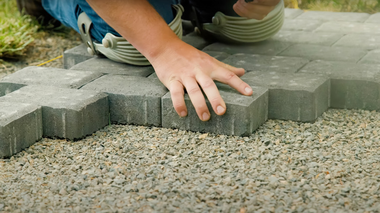 A person wearing knee covers installing concrete paver blocks on a bed of gravel