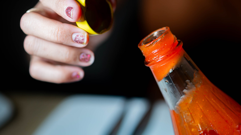 Closeup of a hand opening a bottle of hot sauce