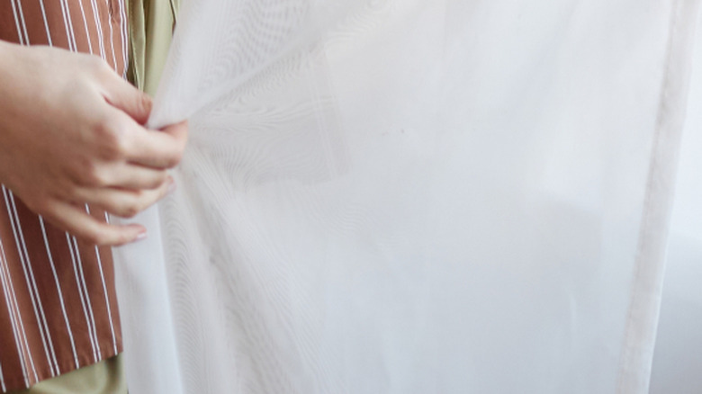 hand holding a sheer white curtain