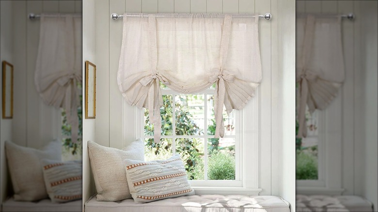Window nook with white linen curtains and cushioned bench with throw pillows