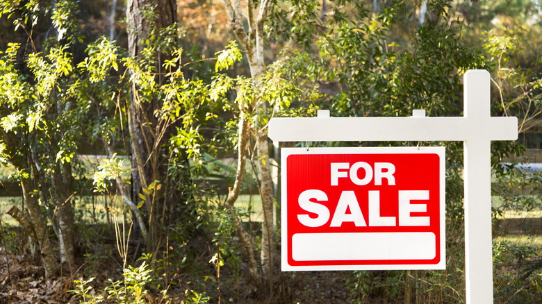 A red "for sale" sign in front of a vacant lot