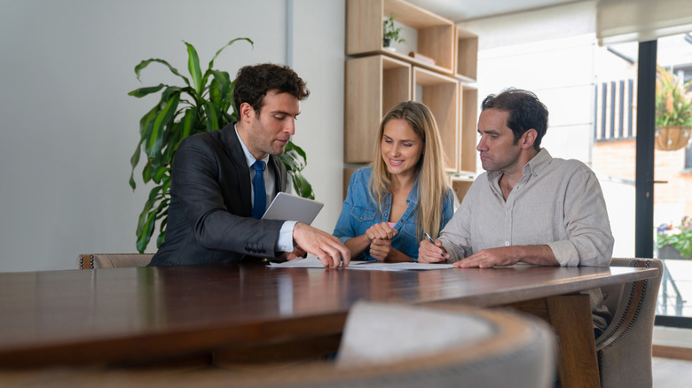 A happy couple sitting in a home with an agent and signing the house deed