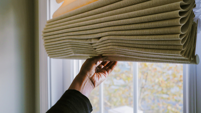 Hand adjusting shade over window