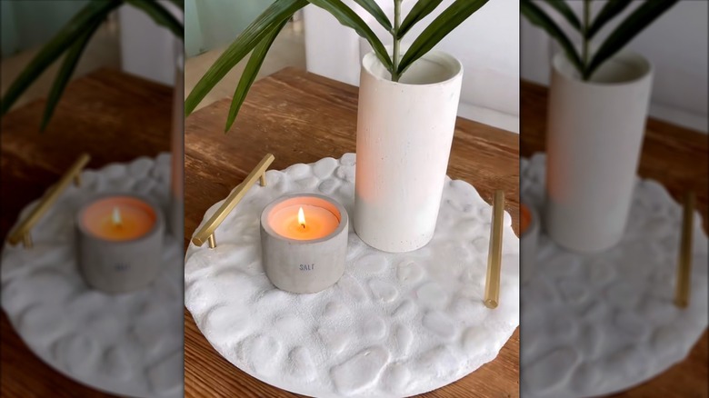 A round tray mosaiced with river stones sits under a vase and candle on a coffee table.