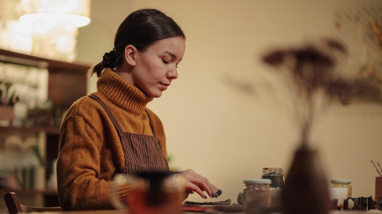 A dark-haired woman concentrates on a crafting project.