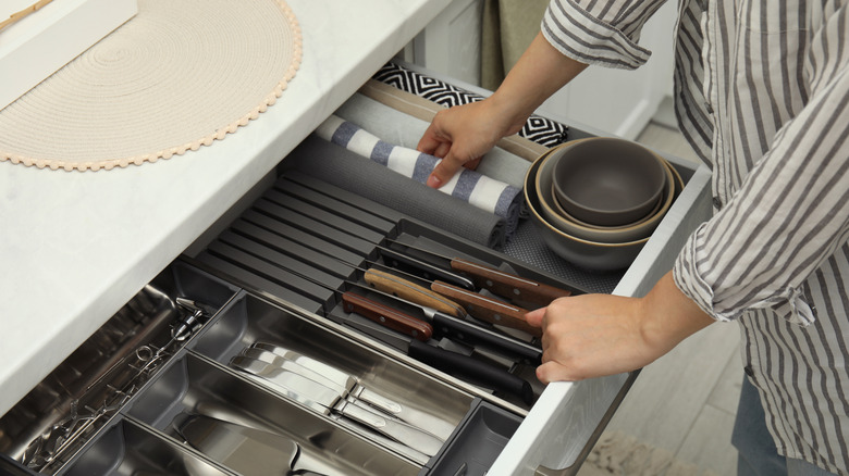 A person with a white and brown striped shirt organizing a kitchen drawer