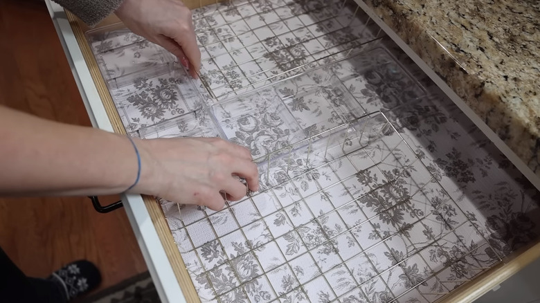 Hands moving around clear and mesh organizers on a vinyl-lined drawer