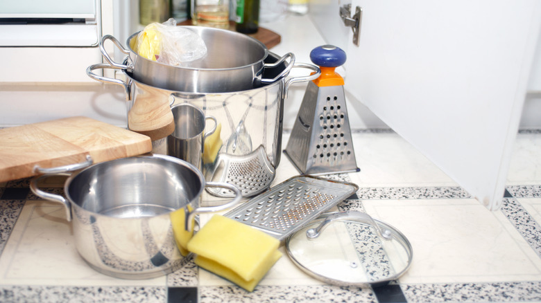 A cutting board and other kitchen utensils messily spilling out of a kitchen cabinet.