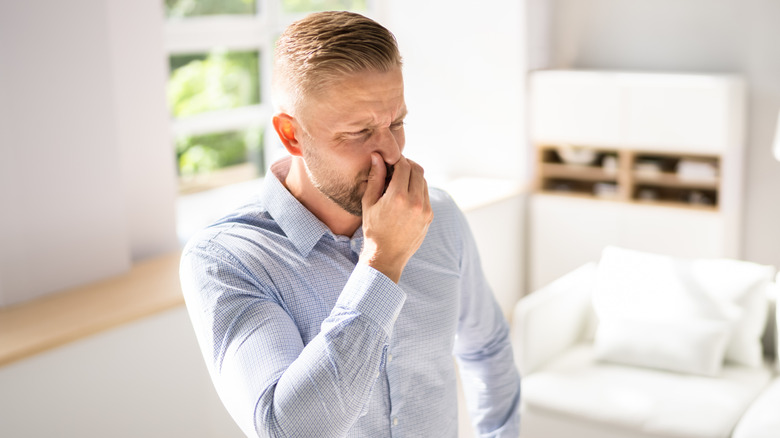 Man wearing dress shirt holding his nose because of bad smell