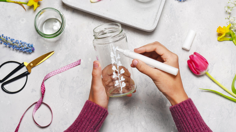 Hands painting a glass jar with flowers and scissors