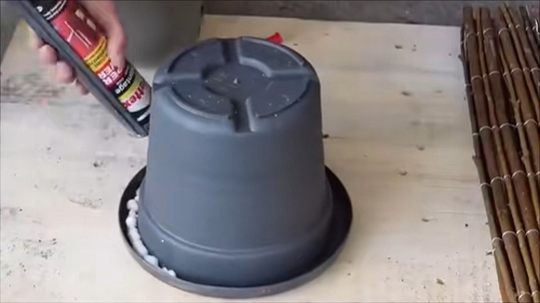 A person's hand applies silicone glue to the inner lip of a plastic plant pot.