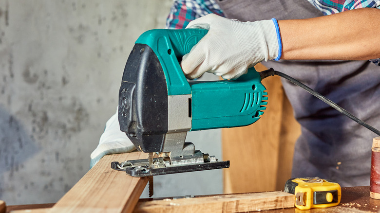 An electric jigsaw tool cutting through a wooden board