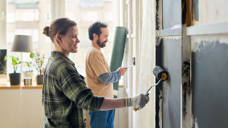 Two people work on a diy home renovation project using green paint and trim on the walls