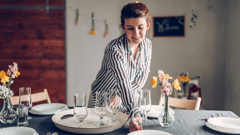 A woman decorating a dining table with wine glasses and dishware.