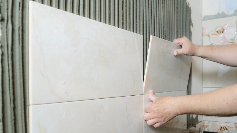 Large marble tiles are being installed on a bathroom wall.