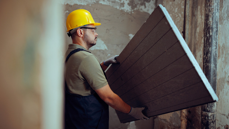 A contractor in a yellow construction hat examines a backer board he's preparing to install.