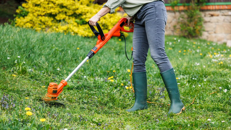 Woman holding a weed eater in a yard