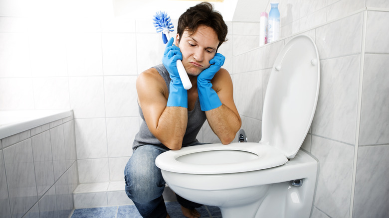 Man squats next to toilet with brush