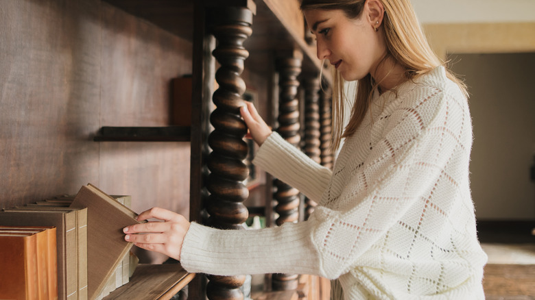 Woman pulling book on wooden shelf