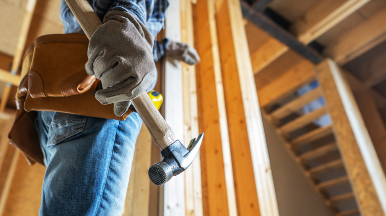 A construction worker holding a hammer and preparing to frame a wall
