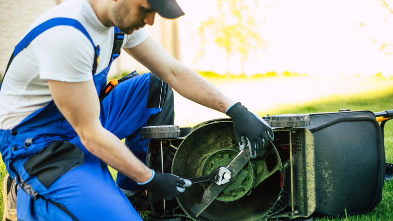 Young guy outside fixing as lawn mower that's lying on its side