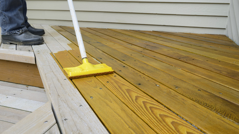 Someone applying wood stain to a deck using a sponge brush.