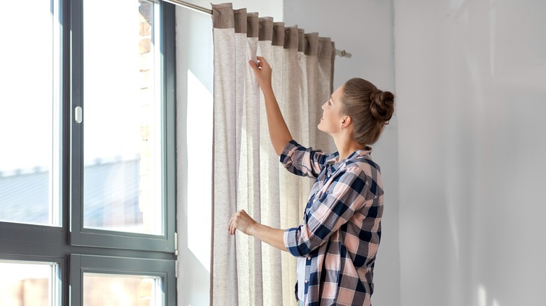 woman arranging curtains on window
