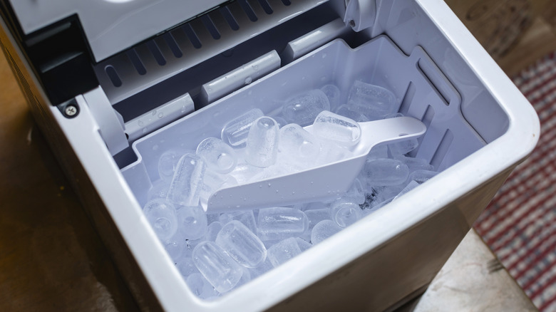 An ice maker with ice and a plastic scooper